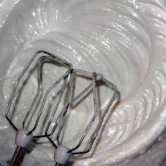 Pair of steel hand mixer beaters whipping glossy egg whites to stiff peaks in a bowl