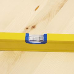 Yellow spirit level with a bubble vial lying on a pale pine board