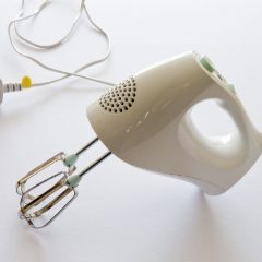 Cream electric hand mixer with two steel beaters fitted, lying on a white surface with its cable and plug