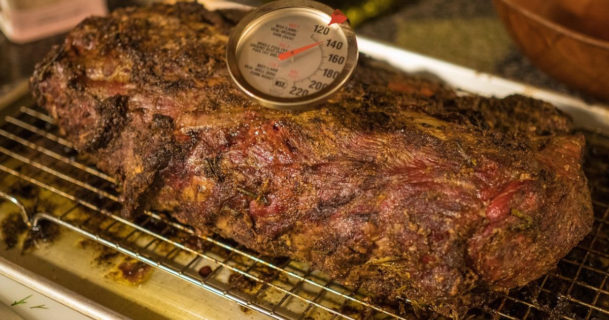 Roast beef resting on a rack with a dial meat thermometer in it