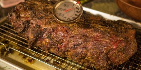 Roast beef resting on a rack with a dial meat thermometer in it