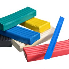 Teal, yellow, blue, white, black and red modelling clay bars with a blue modelling tool on white