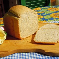 Tall bread-machine loaf cut open on a wooden board, slices beside it, on a sunflower tablecloth