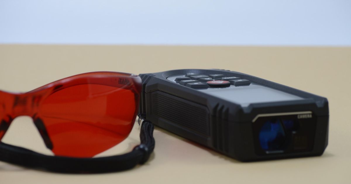 A black laser distance meter beside red laser safety glasses
