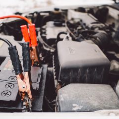Red and black clamps connected to a car battery's terminals in a bright engine bay