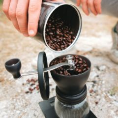 Pouring coffee beans into a black hand grinder with a crank