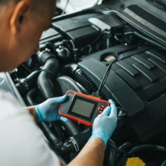 Gloved hands holding a red handheld code reader over an engine