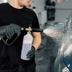 A black pressure washer gun with a foam bottle spraying a blue car