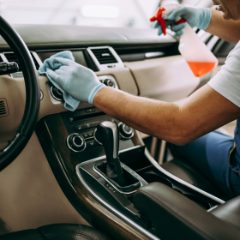A gloved hand wiping a car dashboard with a cloth and spray