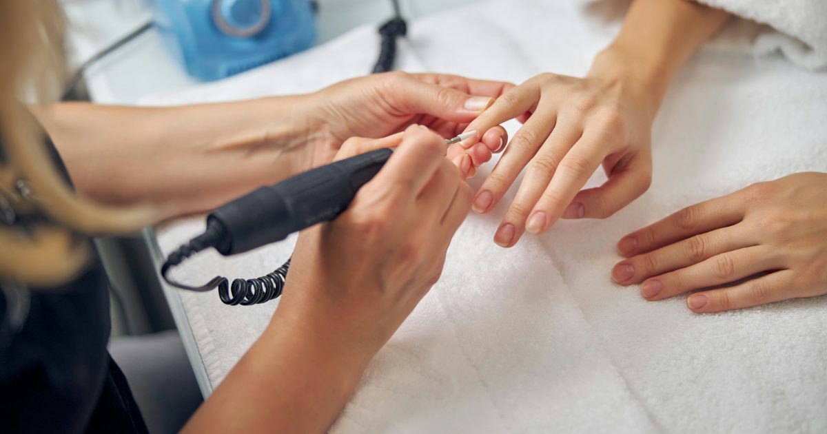 A nail technician shaping a client's nails with an electric nail drill