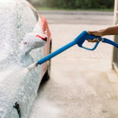 A blue pressure washer gun spraying foam off a red car
