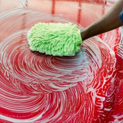 A green microfibre mitt washing a soapy red car