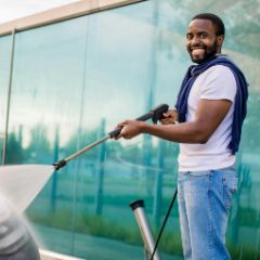 A smiling man pressure washing with a long black lance