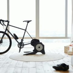 A black road bike on a black direct-drive trainer in a bright room with big windows