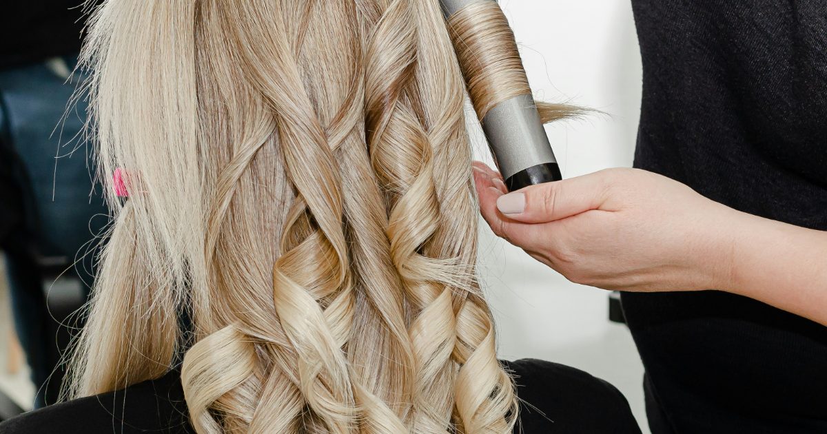 A stylist curling long blonde hair into soft ringlets with a curling wand