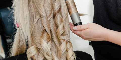 A stylist curling long blonde hair into soft ringlets with a curling wand