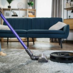 A purple and grey stick vacuum on a rug in a bright living room
