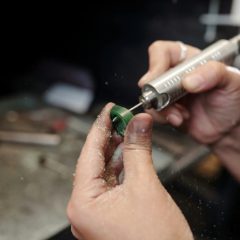 A slim rotary tool shaping a small green piece with a grinding bit
