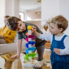 Two young children playing with a colourful ball run tower at home