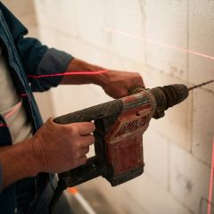 Hands drilling into a block wall along a red laser line