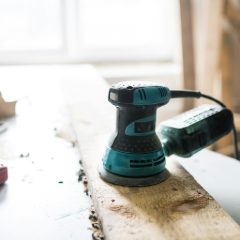 A teal-green sander resting on a wooden board in a workshop
