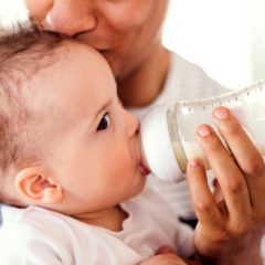 Father kissing his baby son's head while feeding him from a clear bottle