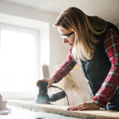 A woman sanding a board in a bright workshop