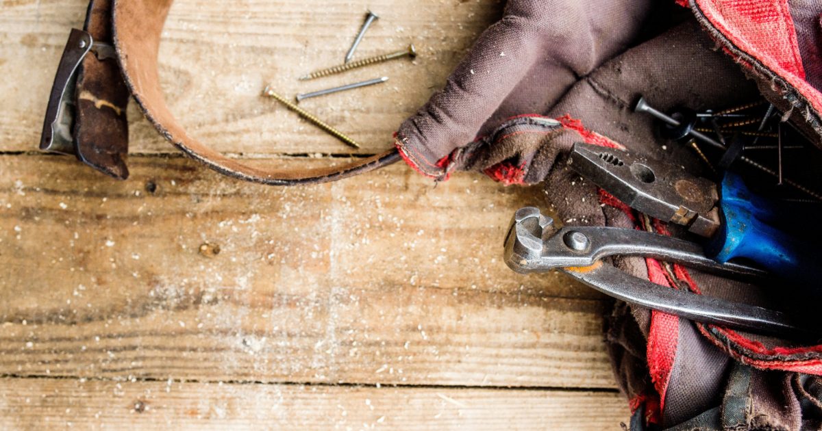 A well-used canvas tool bag spilling pliers and screwdrivers onto a wooden workbench