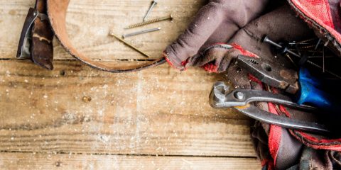 A well-used canvas tool bag spilling pliers and screwdrivers onto a wooden workbench