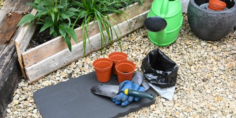 A gray kneeling mat on gravel beside pots, gloves and a watering can