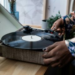 Hands lowering the arm onto a record on a fabric-fronted turntable