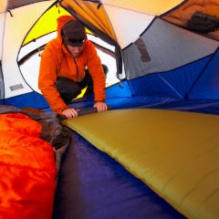 Man in an orange jacket laying a self-inflating mat inside a bright orange and blue dome tent