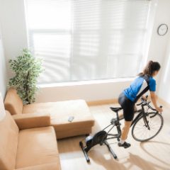A cyclist riding a road bike on a black direct-drive trainer in a bright living room