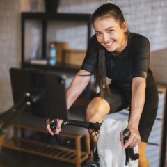 A smiling cyclist riding an indoor trainer at home with a tablet on the handlebars