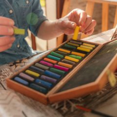 Picking a pastel from a wooden box of rainbow colours