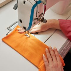 Hands sewing orange fabric on a white sewing machine with a turquoise stripe