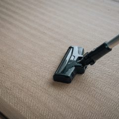 A dark stick-vacuum head on a herringbone carpet
