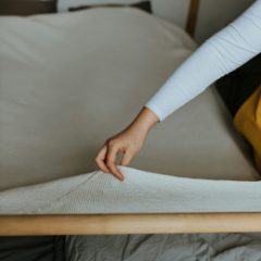 A woman lifting the corner of a foam mattress topper on a bed