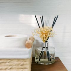 A round glass reed diffuser with dried flowers and black reeds in a bathroom