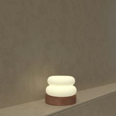 A small white glowing lamp on a wooden base on a shelf
