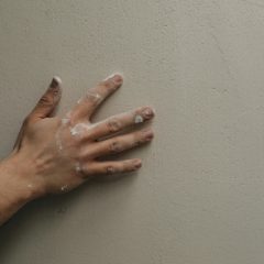 A hand pressed flat against a pale plastered wall