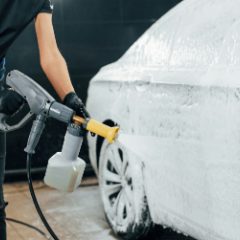 A pressure washer gun with a yellow foam nozzle covering a car in suds