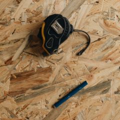 A black tape measure and a carpenter's pencil on a sheet of chipboard