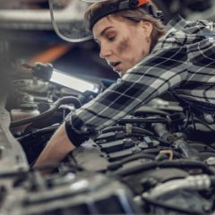 Mechanic in a checked shirt and head torch working in an engine bay, a long LED light bar hanging under the bonnet