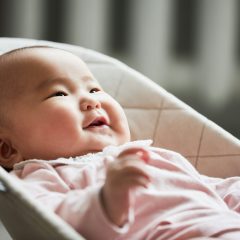 Laughing baby in pink lying in a light grey fabric bouncer