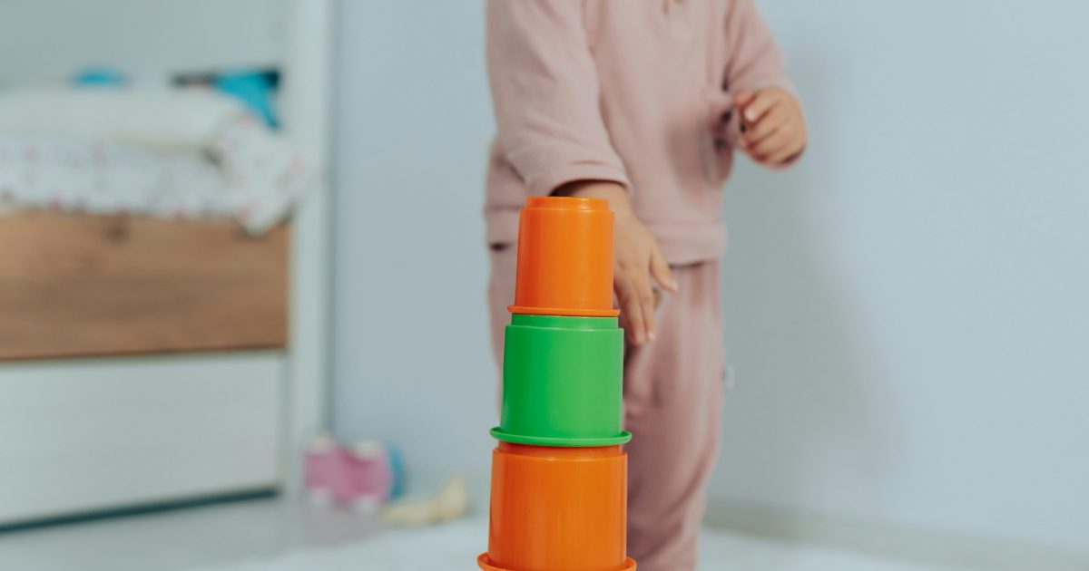 A toddler building a tower of stacking cups in a bright bedroom