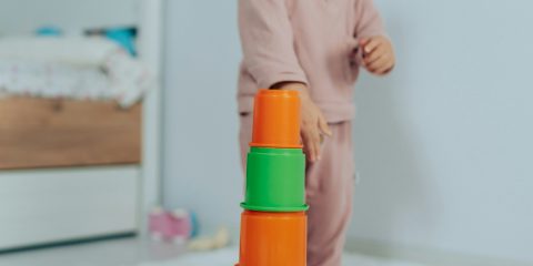 A toddler building a tower of stacking cups in a bright bedroom