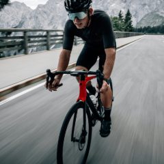 A cyclist in a black helmet riding a road bike along a mountain road