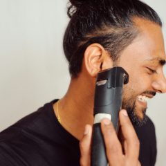 A smiling man trimming near his ear with a black trimmer