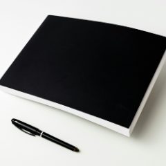A black pen beside a black notebook on white